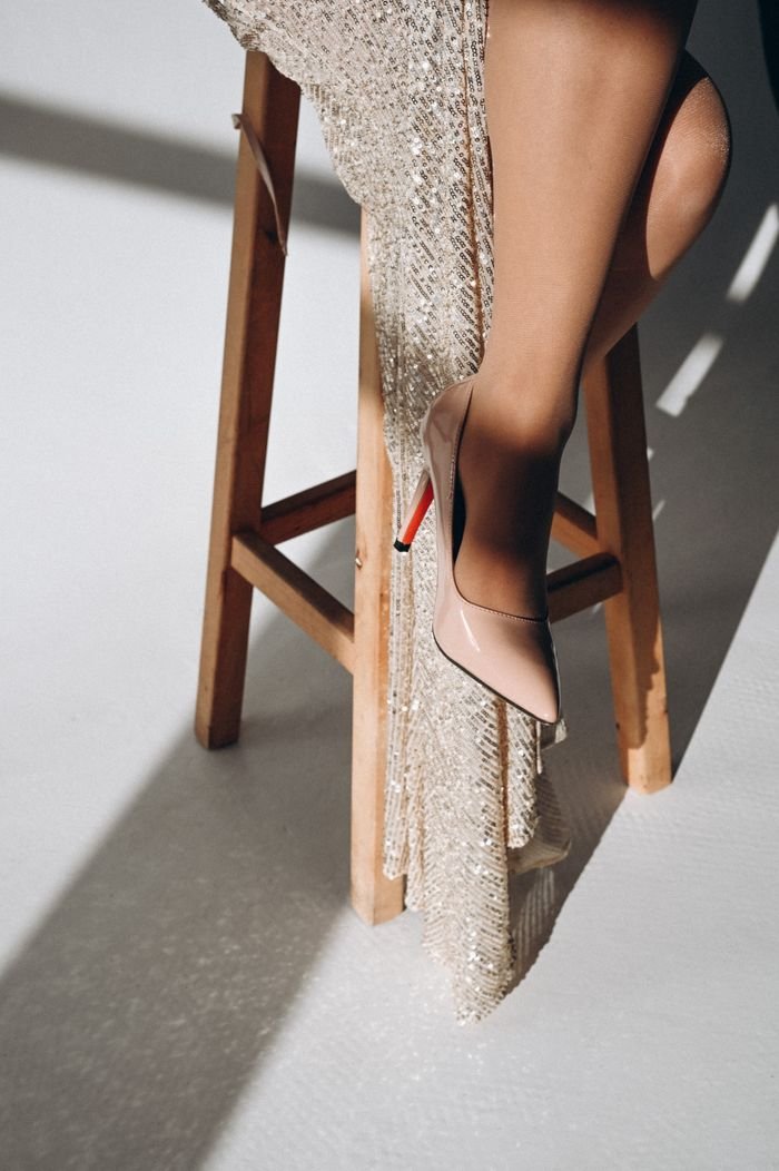Close-up of a woman's legs in a sparkling evening gown with high heels on a wooden stool.