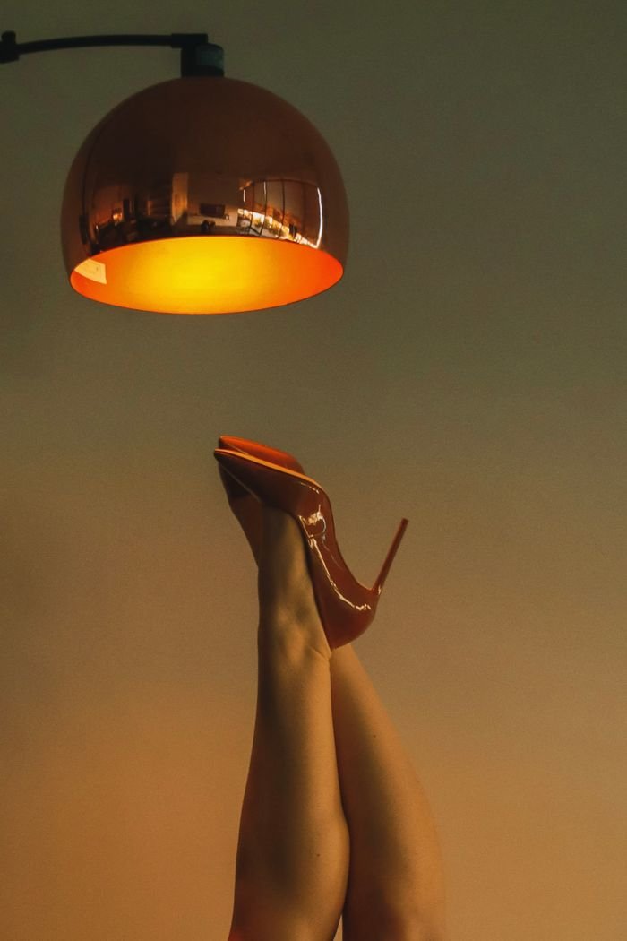 Artistic shot of legs in red high heels raised under a warm glowing lamp.