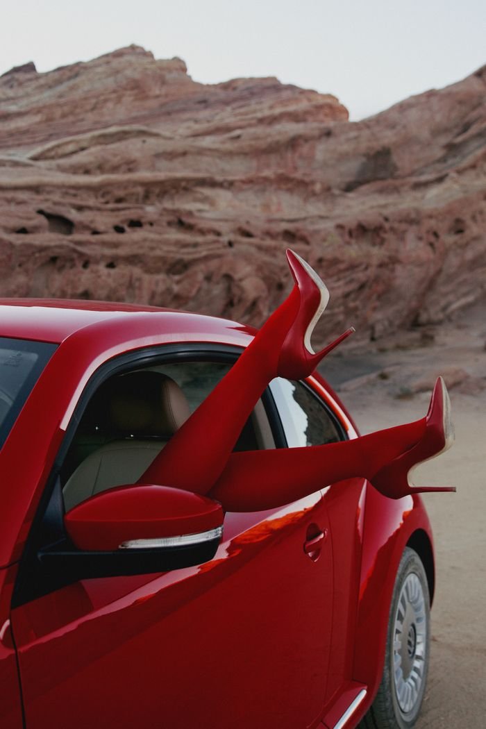 Red sports car with legs in high heels against a desert backdrop.